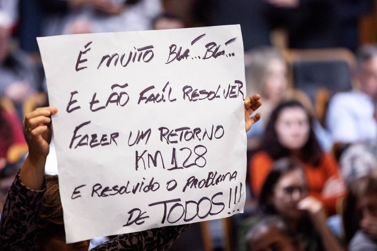 Cidadão ergue cartaz manuscrito durante assembleia pública
